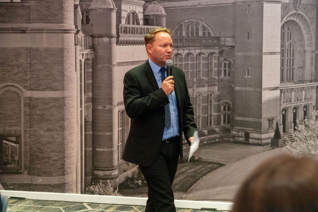 Andy Allford dressed in a suite at the Hall of Fame, speaking into the mic.