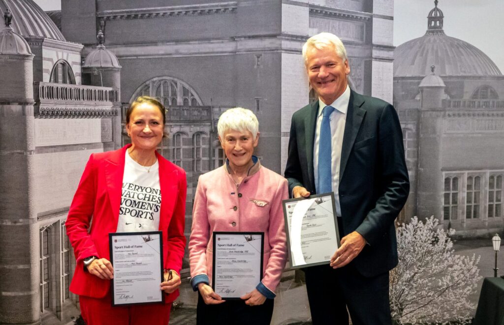 Three inductees at the Hall of Fame, all dressed in smart attire, particularly suits, holding their certificates.