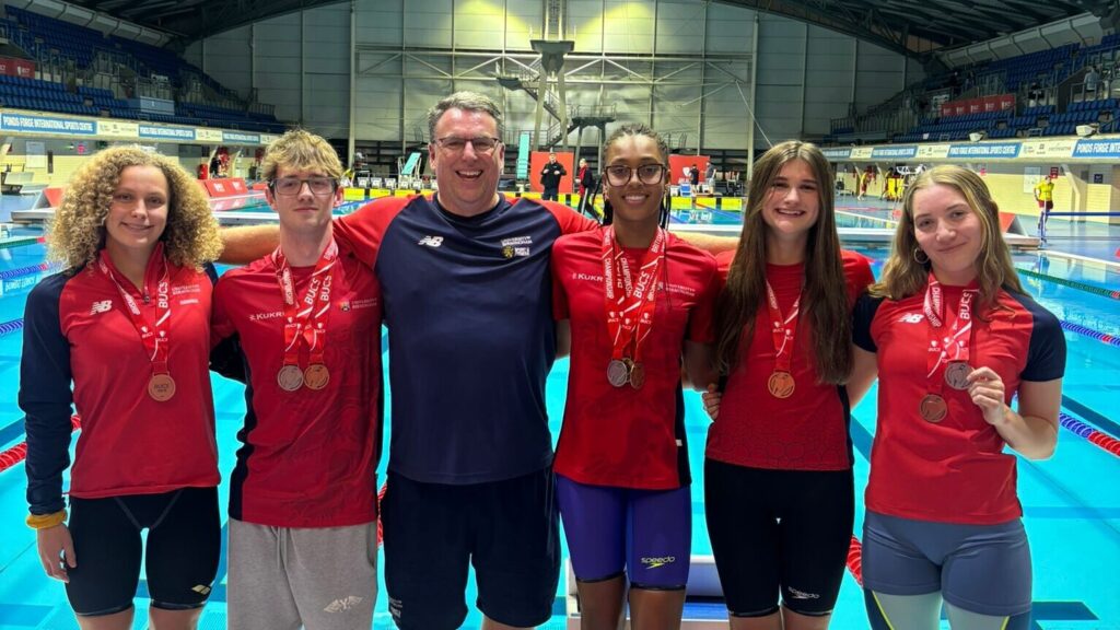 University of Birmingham Swimmings standing in front of a pool with their medals, they are smiling.
