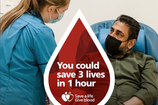 Man donating blood at blood drive, supported by nurse.